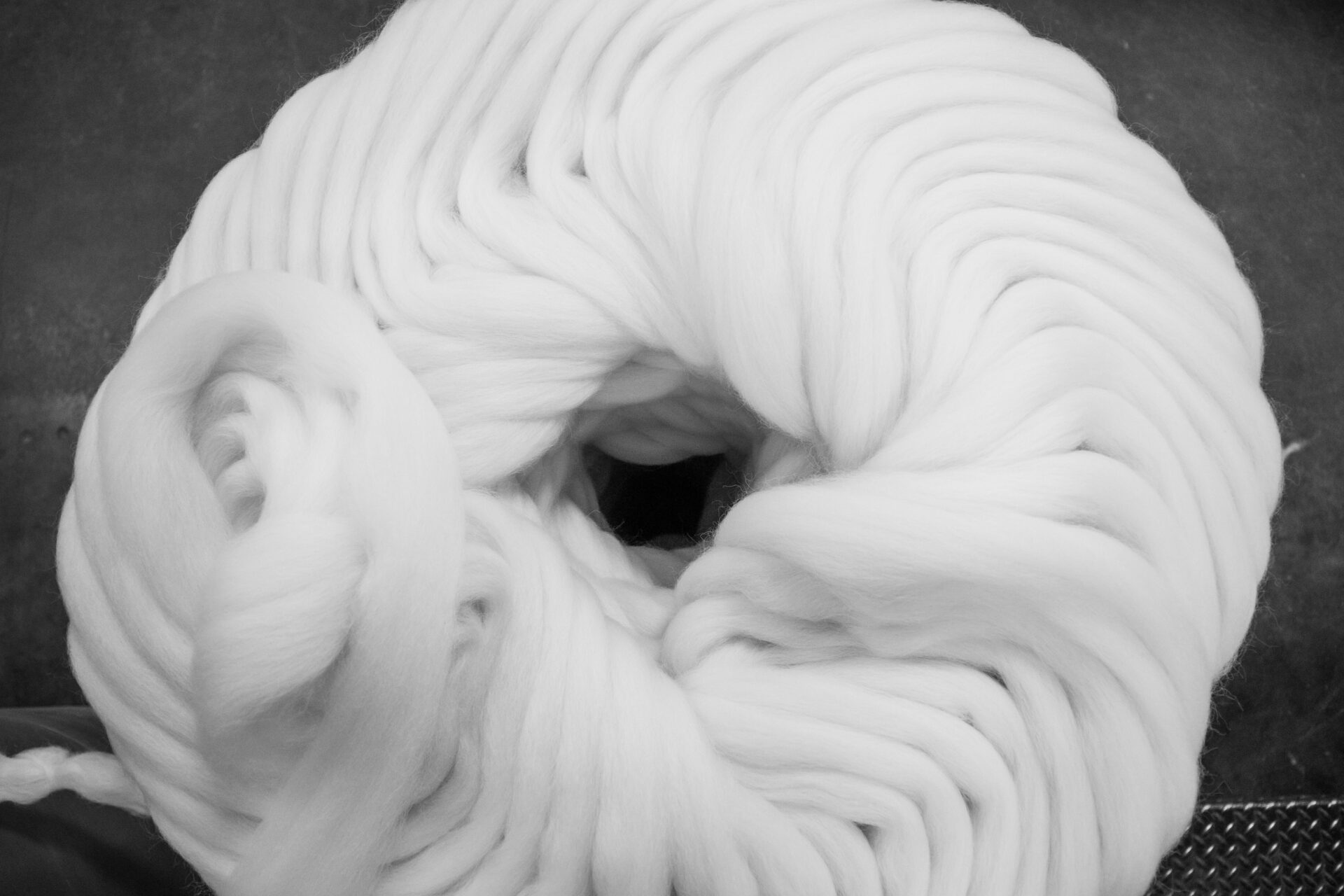 Thick white wool yarn coiled into a circular skein on a dark background
