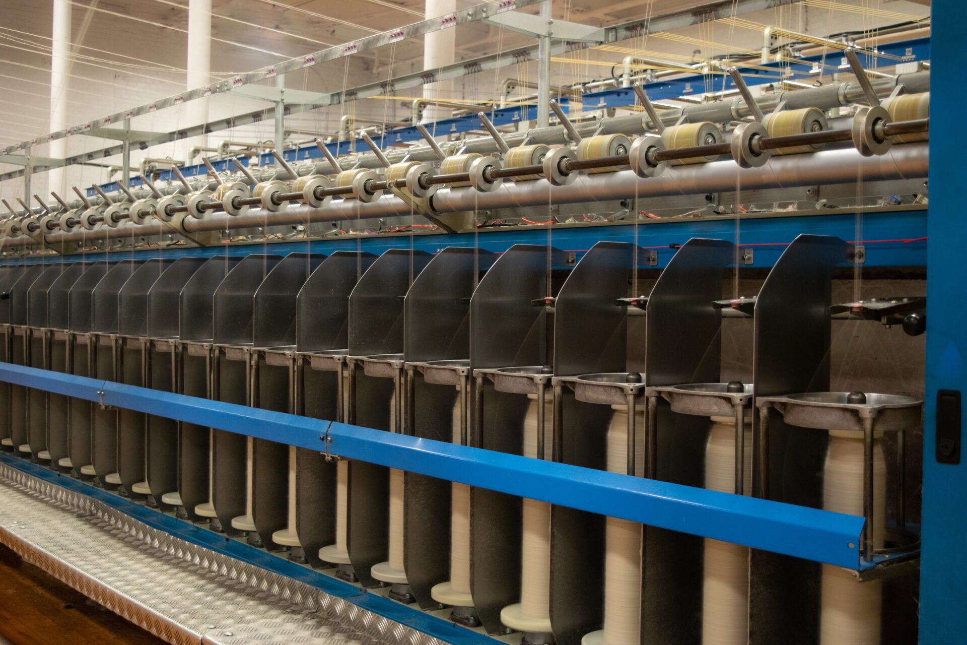 Ranlo_plant 1 - Meridian Specialty Yarn Group Row of large spools on a textile machine with metal separators in a factory setting